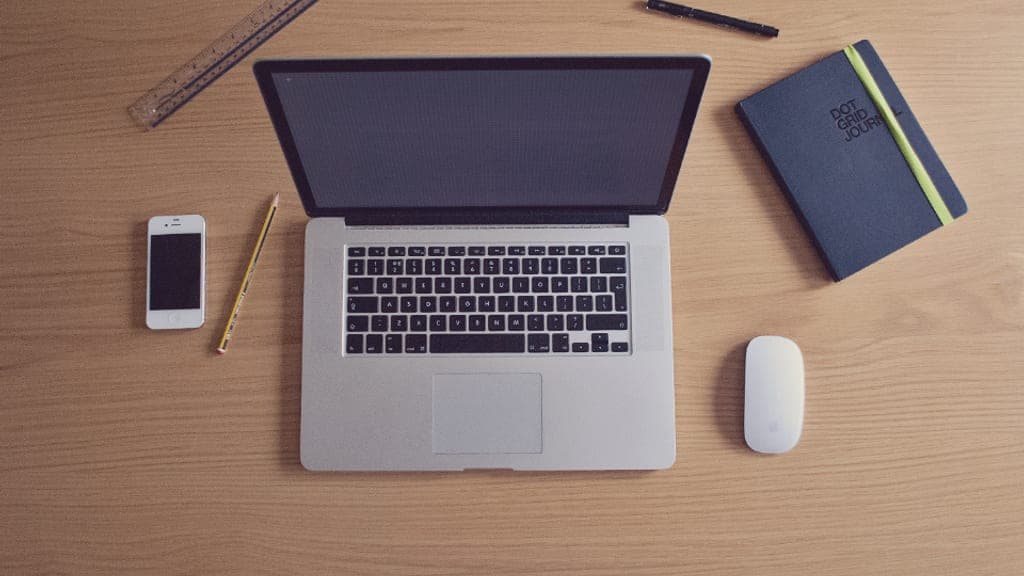 Ordinateur portable ouvert sur un bureau en bois, entouré d’un carnet, d’un téléphone et d’un stylo