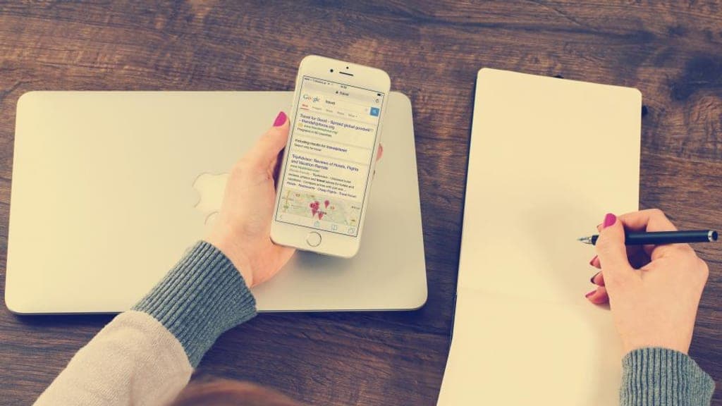 Personne consultant un moteur de recherche sur son téléphone tout en prenant des notes sur un carnet