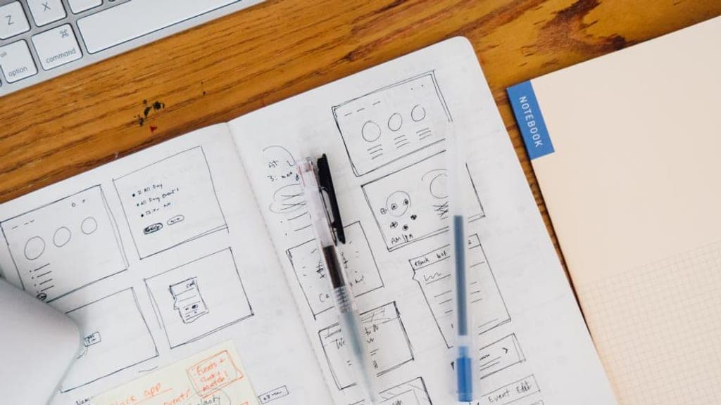 Carnet ouvert couvert de croquis de pages web dessinés à la main, posé sur une table en bois